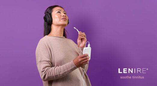 Image of a woman wearing headphones. She is holding a Lenire device in her hands.