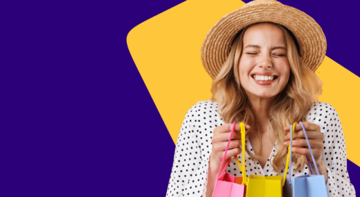 Lady with long blonde hair wearing a straw hat. She is smiling with her eyes closed. She is holding three shopping bags.